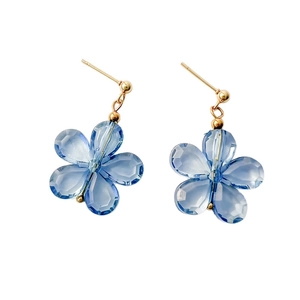 Boucles d'oreilles fleurs en cristal bleu avec clous dorés sur fond blanc épuré