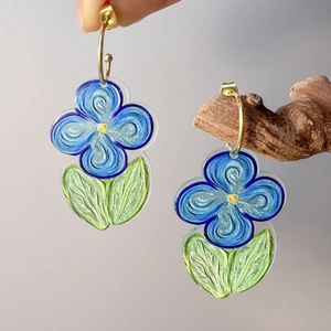 Detail of floral earring with blue petals and green leaves on golden ring