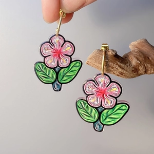Detailed close-up of colorful floral earrings with pink petals and gold C-shaped hoops