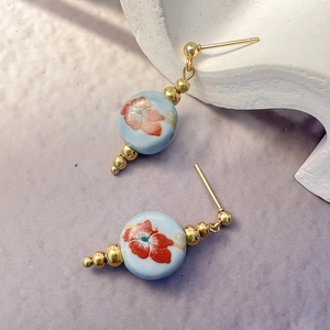 Detail of blue ceramic stud earrings with red floral patterns and gold accents