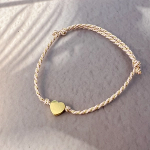 Pink and gold woven cord bracelet with a polished golden heart pendant and leaf shadow