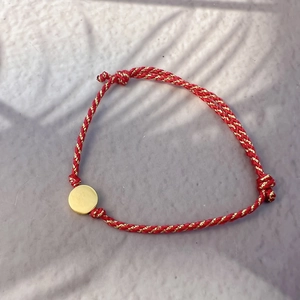 Detail of red and gold braided rope bracelet with a round polished golden metal charm