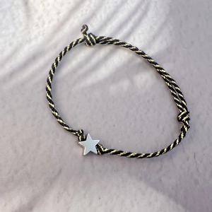 Macro detail of hand-woven black and gold cord bracelet with silver star charm