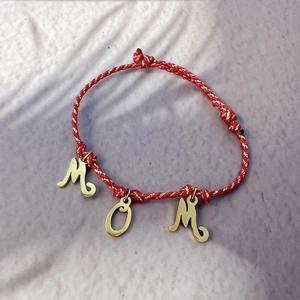 Detail view of MOM letter pendants on red and gold braided rope bracelet for women