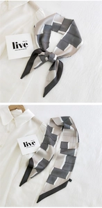 Detail of a narrow silk scarf with geometric gray stripes tied as a stylish fashion accessory