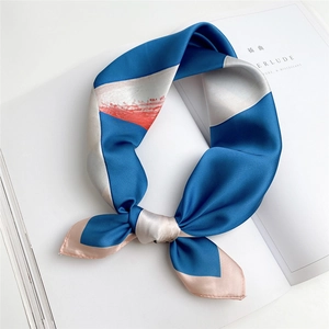 Elegant blue silk square scarf with geometric patterns tied on a white magazine