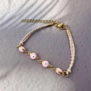 Dettaglio del bracciale rosa malocchio intrecciato con perle dorate e catenella