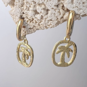 Goldene Edelstahl-Ohrringe mit gehämmerter Palme und Anhänger auf weißem Stein