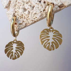 Detailansicht goldener Monstera-Blatt-Ohrringe an einem weißen Stein-Hintergrund