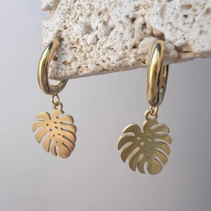 Detail der goldenen Monstera-Ohrringe auf weißem Stein mit matter Textur und poliertem Reif