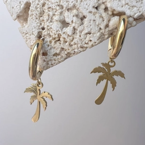 Makro-Detail goldener tropischer Palmen-Ohrringe auf einem natürlichen Mineralsteinsockel