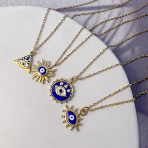 Close-up of golden evil eye necklaces with colorful enamel pendants on a stone base