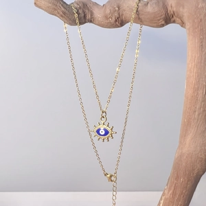 Vintage evil eye necklace with gold chain on wooden branch against gray background