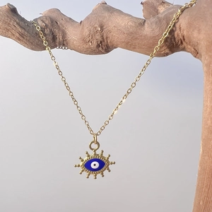 Close-up of golden evil eye necklace pendant draped over natural wood texture