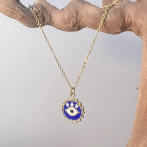 Detail of golden Evil Eye necklace pendant with blue enamel hanging on a wooden branch