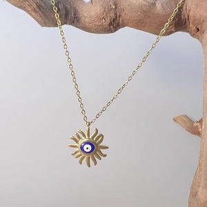 Detail of vintage gold evil eye sun pendant on a dainty chain with rustic wood background