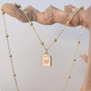 Détail de la chaîne à billes dorée et pendentif papillon en émail rose sur branche