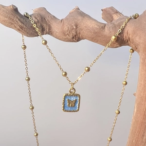 Détail du pendentif en émail bleu carré avec papillon doré sur présentoir en bois