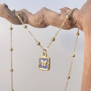 Détail du collier pendentif papillon doré carré avec émail bleu sur branche en bois
