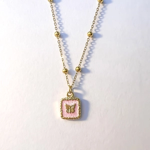 Détail macro d'un pendentif papillon doré avec émail rose sur un collier à perles