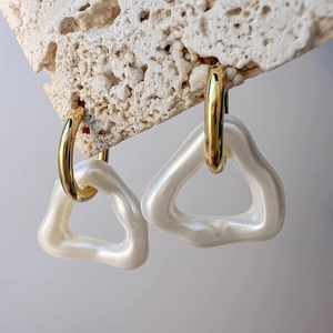 Detailed macro of gold geometric earrings with pearl-white irregular triangle pendants