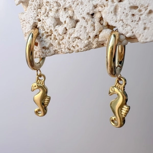 Macro view of gold seahorse pendant earrings on coral rock with marine aesthetic