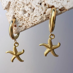 Macro view of golden starfish charm huggie earrings on white volcanic stone background
