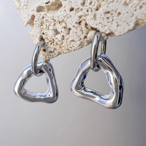 Close-up of geometric silver triangular earrings hanging on a textured stone prop
