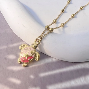 Detail of a turtle pendant with pink enamel and starfish charms on a gold beaded chain