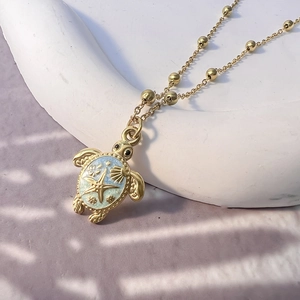 Detailed macro view of 18K gold sea turtle necklace with blue enamel and starfish patterns