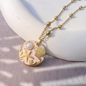 Detailed macro of ocean-themed necklace with pink enamel starfish pendant and pearl charm