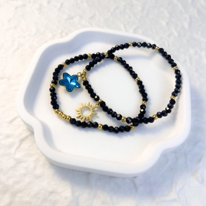 Detail of black beaded bracelets with blue star and gold sun charms on ceramic tray