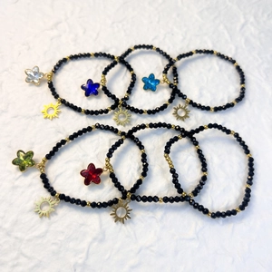 Elastic beaded bracelet with black glass beads, golden sun charms and colorful star charms