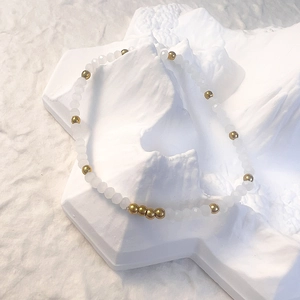 Detail of white faceted beads and gold spacers draped over a white mountain stand