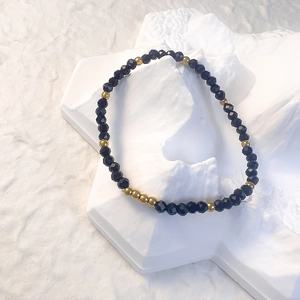Close-up of black faceted glass beads and gold metal spacers on a white textured background