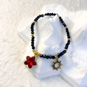 Detail of black glass beaded elastic bracelet with gold sun charm and red star pendant