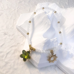 Detail of white beaded bracelet with gold sun charm and green star pendant on stone base