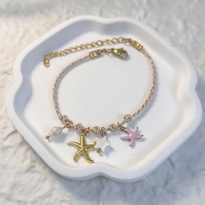 Detailed view of woven rope bracelet with pearl, starfish pendants and lobster clasp