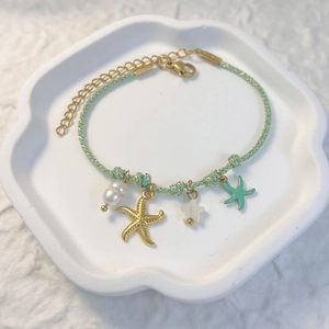 Detail of mint green woven rope bracelet with gold starfish and pearl charms