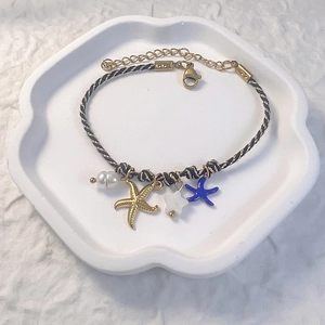 Detail of woven bracelet with golden starfish, pearls, and blue charms on a white tray