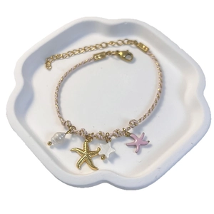 Ocean-themed pink braided cord bracelet with starfish, pearl and coral charms on a tray