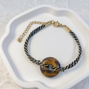 Close-up of a woven bracelet with a faux amber donut charm on a white ceramic tray