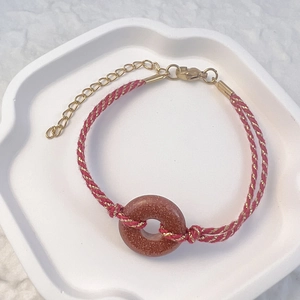 Detail of red and gold woven bracelet with tiger eye stone and stainless steel clasp