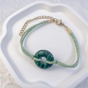 Macro detail of hand-woven green malachite stone bracelet with golden lobster clasp