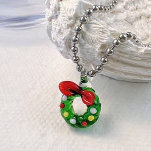 Détail d'un pendentif couronne de Noël en verre vert sur collier chaîne à billes