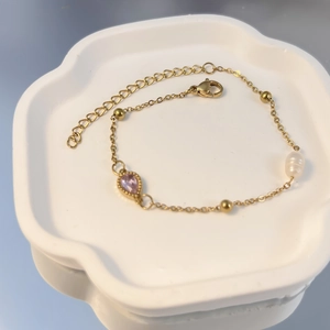 Detail eines vergoldeten Armbands mit rosa Tropfen-Zirkon und weißer Barockperle