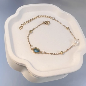 Detail eines vergoldeten Armbands mit blauem Wassertropfen-Edelstein und weißer Perle