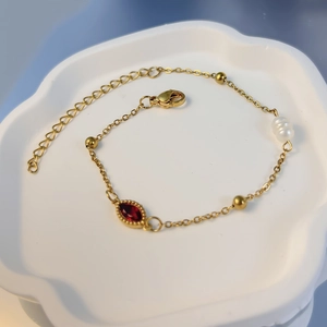 Detailansicht eines vergoldeten Armbands mit rotem Zirkonia und Perle in einer Keramikschale