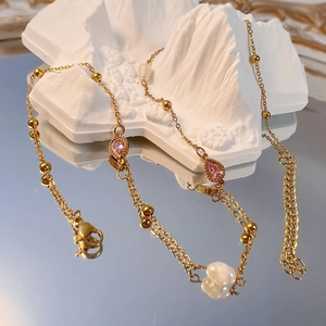 Dettaglio di una collana dorata con zircone rosa a goccia e perle barocche su fondo specchio