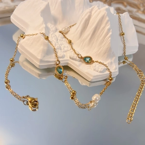 Dettaglio della collana dorata con zircone blu a goccia e perle eleganti